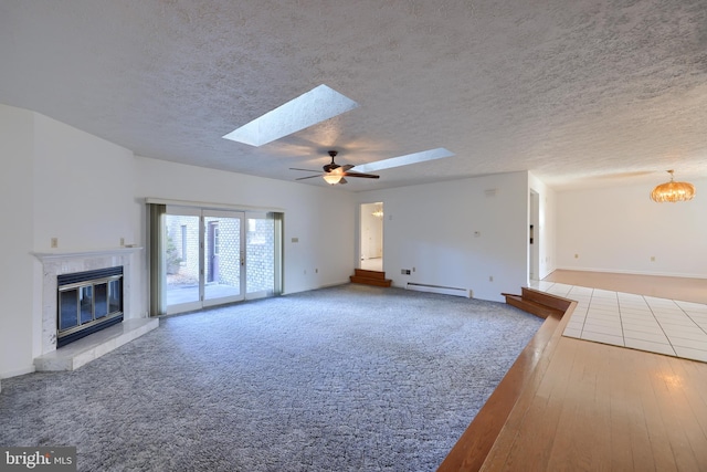 unfurnished living room with baseboard heating, baseboards, a tiled fireplace, ceiling fan with notable chandelier, and a skylight