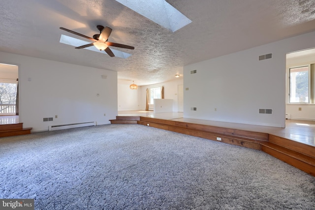 unfurnished living room featuring a skylight, a textured ceiling, visible vents, ceiling fan, and a baseboard heating unit