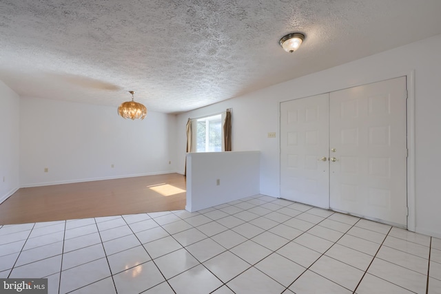 spare room featuring a textured ceiling, a notable chandelier, and baseboards