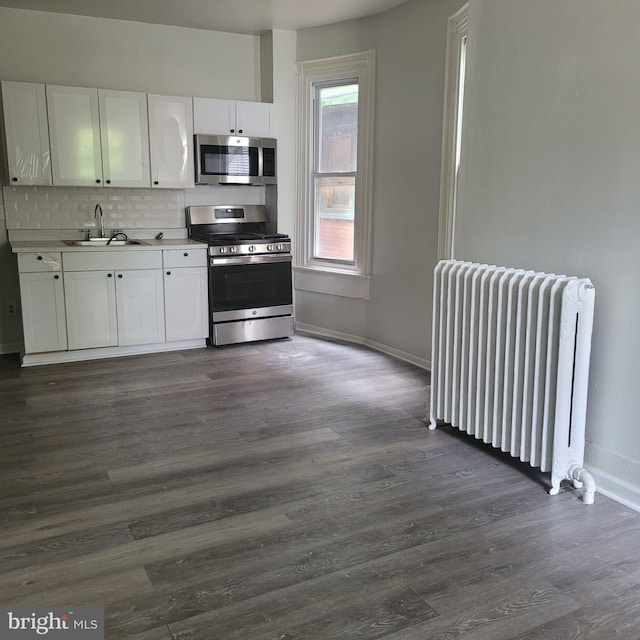 kitchen featuring dark hardwood / wood-style floors, radiator, sink, white cabinetry, and appliances with stainless steel finishes