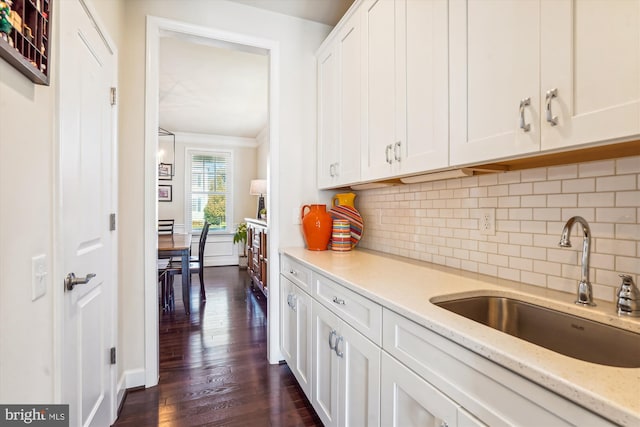 kitchen with white cabinetry, sink, backsplash, light stone counters, and dark wood-type flooring