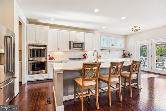 kitchen featuring appliances with stainless steel finishes, a breakfast bar area, a center island with sink, and white cabinets