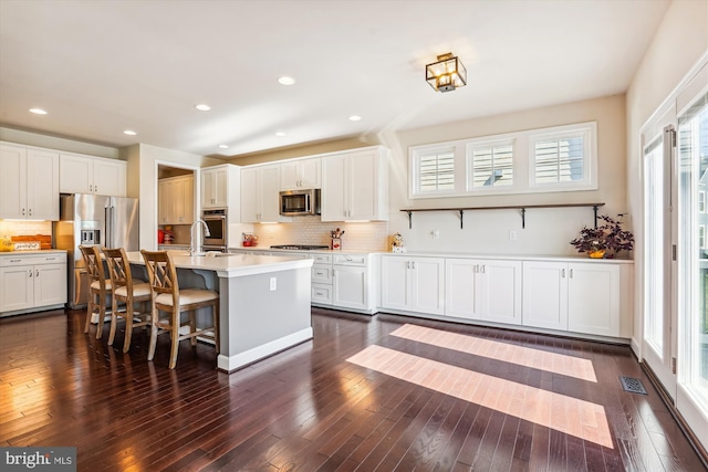 kitchen featuring an island with sink, appliances with stainless steel finishes, dark hardwood / wood-style floors, and white cabinets