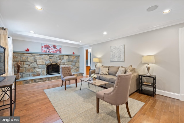 living area with baseboards, a stone fireplace, wood finished floors, and crown molding