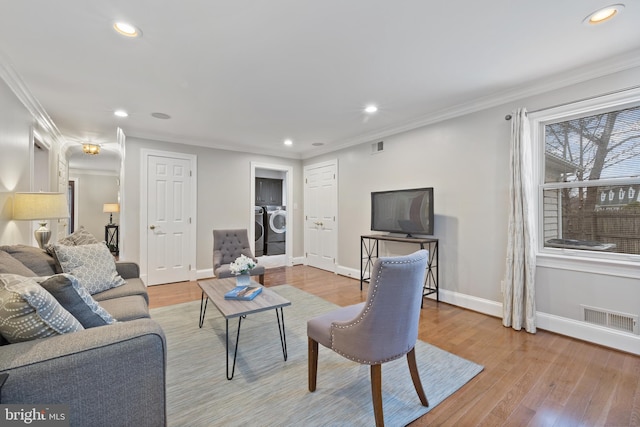 living area featuring crown molding, washer and clothes dryer, visible vents, light wood-style floors, and baseboards