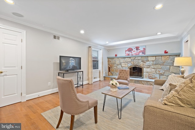 living area featuring a stone fireplace, recessed lighting, wood finished floors, baseboards, and ornamental molding