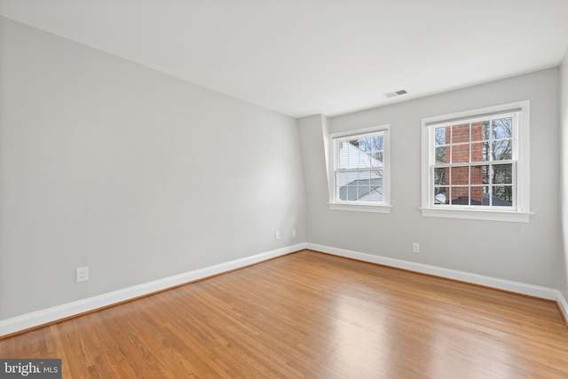 empty room featuring wood finished floors, visible vents, and baseboards