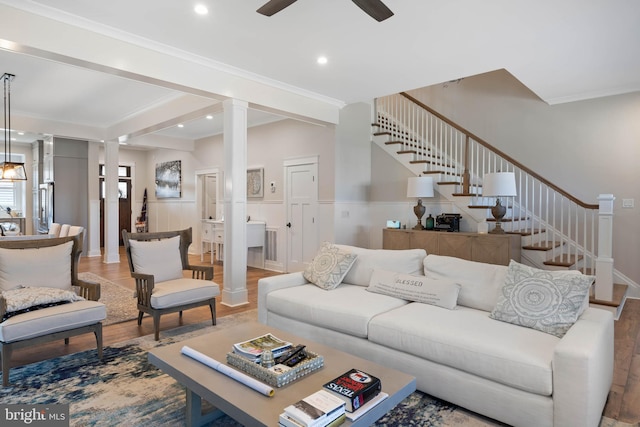 living room featuring wood-type flooring, crown molding, and decorative columns