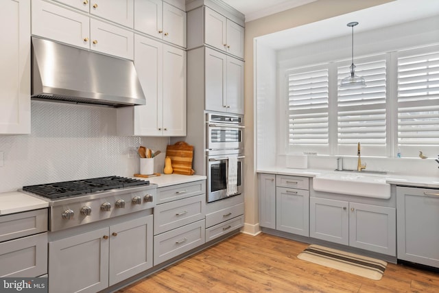 kitchen featuring gray cabinets, appliances with stainless steel finishes, decorative light fixtures, and light hardwood / wood-style flooring