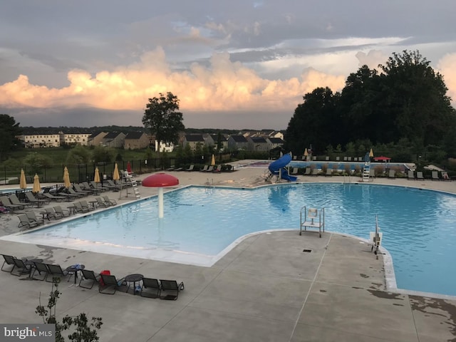 pool at dusk with a water slide and a patio area