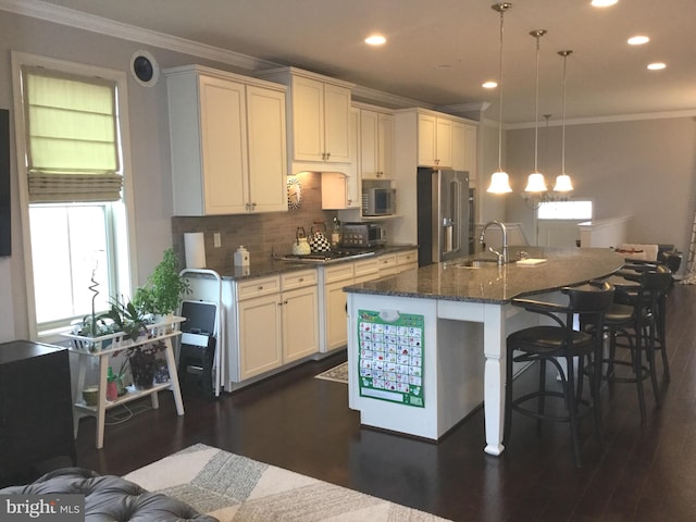 kitchen featuring an island with sink, appliances with stainless steel finishes, dark hardwood / wood-style floors, dark stone countertops, and decorative light fixtures