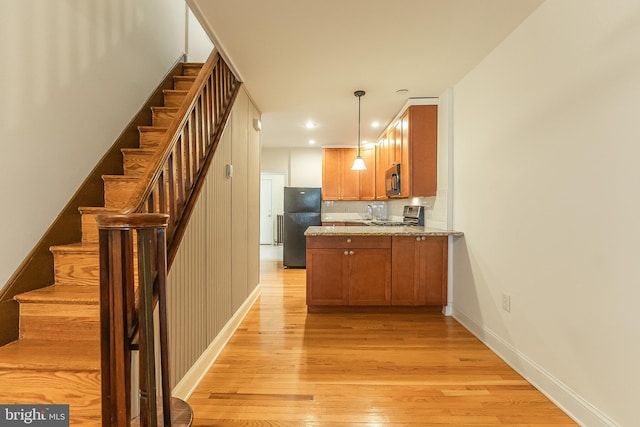 kitchen with decorative backsplash, light stone countertops, black appliances, light hardwood / wood-style floors, and decorative light fixtures