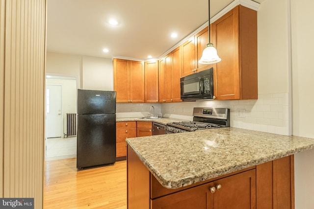 kitchen featuring radiator, light hardwood / wood-style flooring, kitchen peninsula, black appliances, and light stone countertops