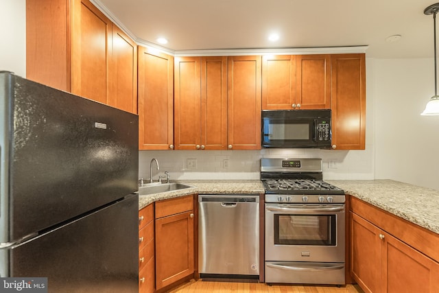 kitchen featuring light stone counters, light wood-type flooring, black appliances, pendant lighting, and sink