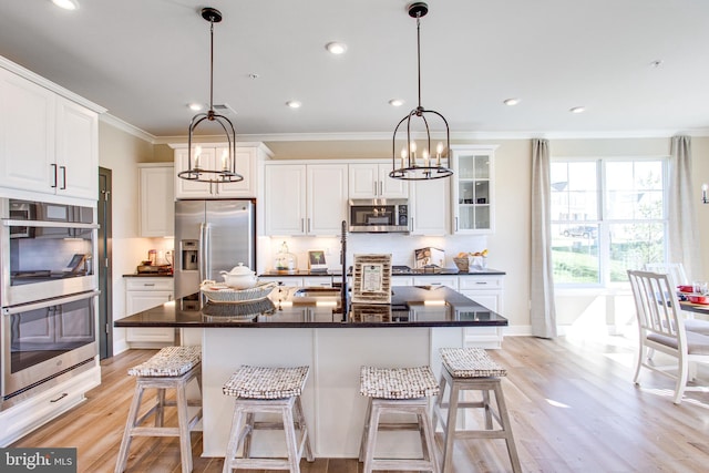 kitchen with white cabinets, hanging light fixtures, appliances with stainless steel finishes, a kitchen island with sink, and light wood-type flooring