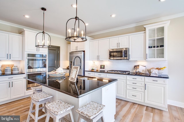 kitchen featuring appliances with stainless steel finishes, white cabinetry, a kitchen island with sink, light hardwood / wood-style flooring, and pendant lighting