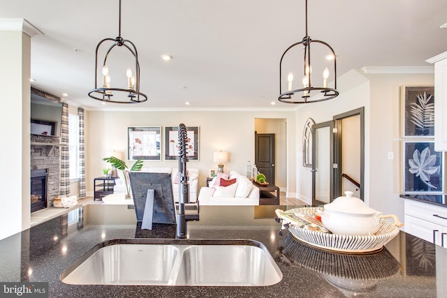 kitchen with a stone fireplace, hanging light fixtures, ornamental molding, and white cabinets