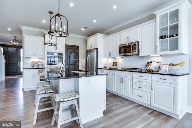 kitchen featuring a breakfast bar area, white cabinetry, a kitchen island with sink, decorative light fixtures, and stainless steel appliances