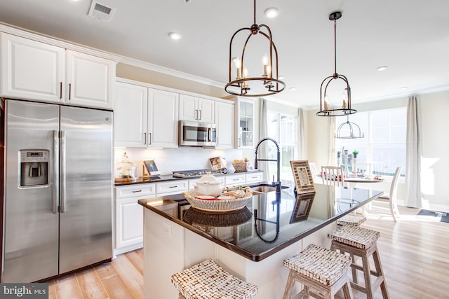 kitchen with appliances with stainless steel finishes, white cabinetry, a kitchen island with sink, and hanging light fixtures