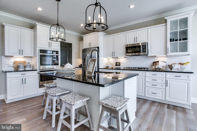 kitchen featuring white cabinets, tasteful backsplash, a center island with sink, light wood-type flooring, and stainless steel appliances