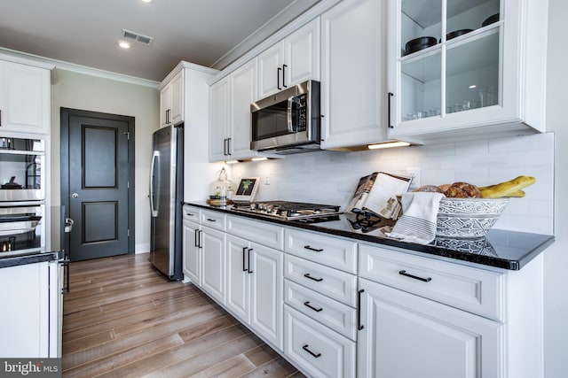 kitchen with stainless steel appliances, crown molding, light wood-type flooring, white cabinets, and tasteful backsplash