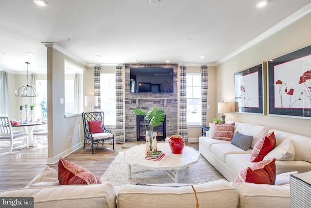 living room with a stone fireplace, ornamental molding, an inviting chandelier, and light wood-type flooring