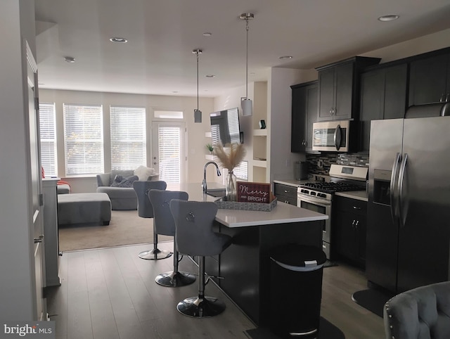 kitchen featuring a kitchen island with sink, hanging light fixtures, wood-type flooring, a kitchen bar, and appliances with stainless steel finishes