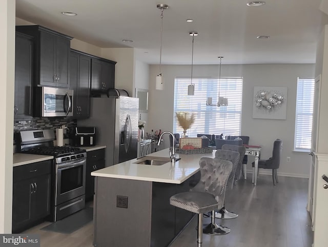 kitchen with a kitchen island with sink, wood-type flooring, sink, pendant lighting, and appliances with stainless steel finishes