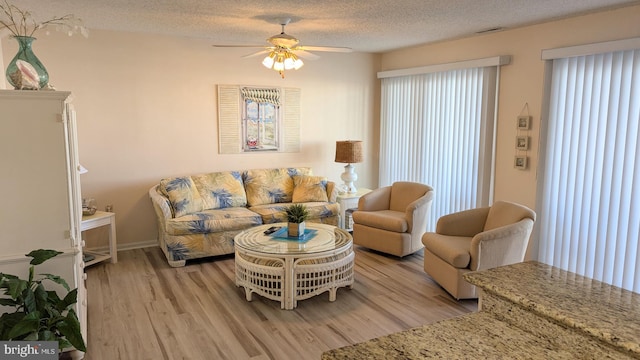 living room with a textured ceiling, light wood-type flooring, and ceiling fan