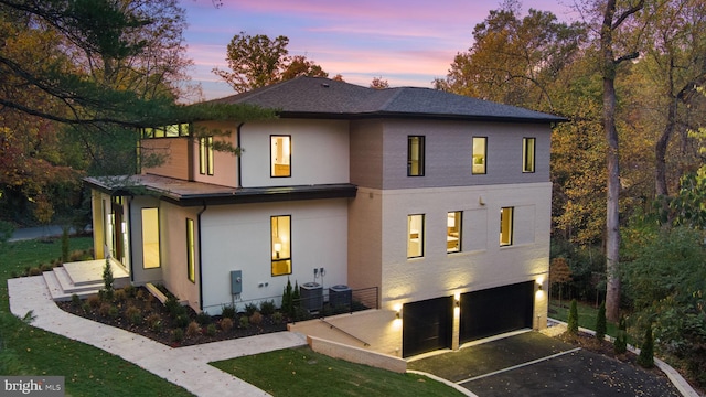 back house at dusk with a lawn, a balcony, and a garage