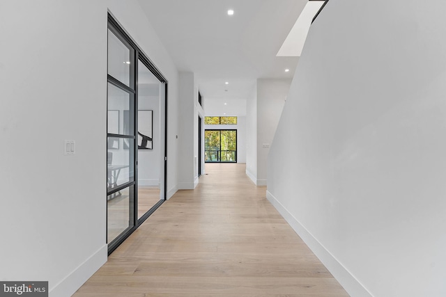 corridor with light hardwood / wood-style flooring and a skylight