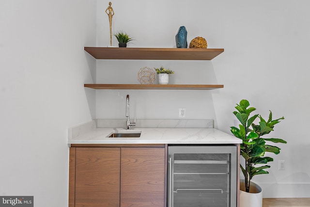 bar with sink, light stone countertops, wood-type flooring, and beverage cooler