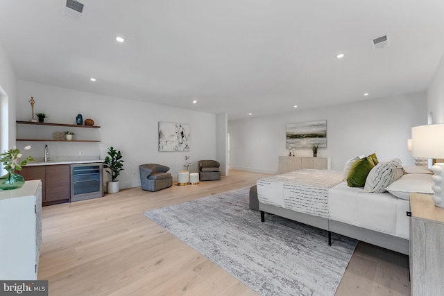 bedroom with light wood-type flooring, bar area, and beverage cooler