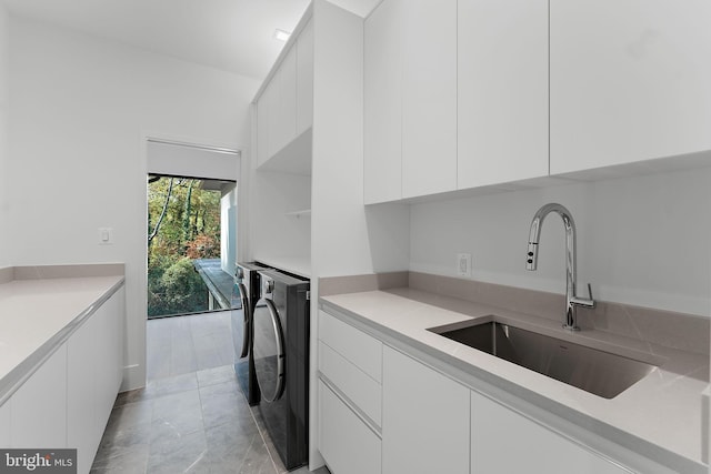 kitchen featuring white cabinetry, sink, light tile patterned floors, and washer and dryer