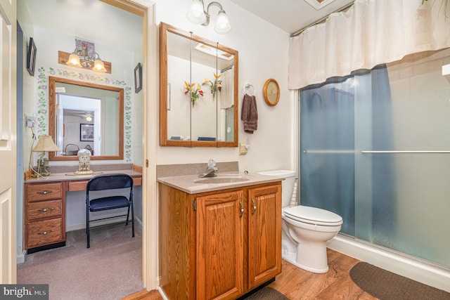 bathroom with toilet, vanity, wood-type flooring, and a shower with door