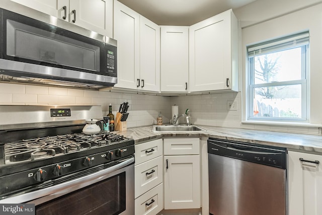 kitchen featuring sink, light stone counters, appliances with stainless steel finishes, white cabinets, and decorative backsplash