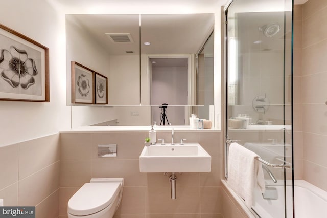 full bathroom featuring toilet, combined bath / shower with glass door, tile walls, and sink