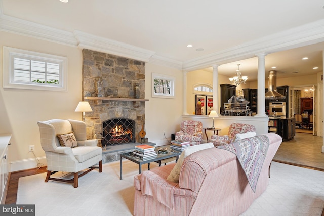 living room featuring ornate columns, a stone fireplace, a notable chandelier, light wood-type flooring, and ornamental molding