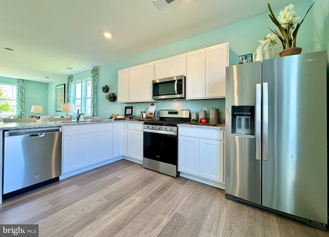 kitchen with white cabinets, appliances with stainless steel finishes, light stone countertops, light wood-type flooring, and sink