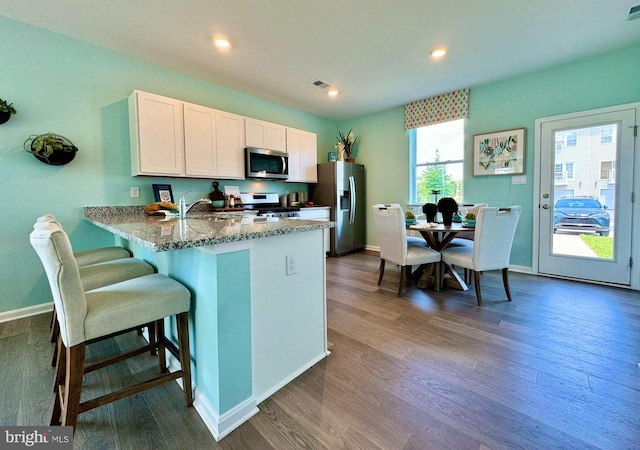 kitchen featuring a kitchen bar, kitchen peninsula, stainless steel appliances, white cabinets, and dark wood-type flooring