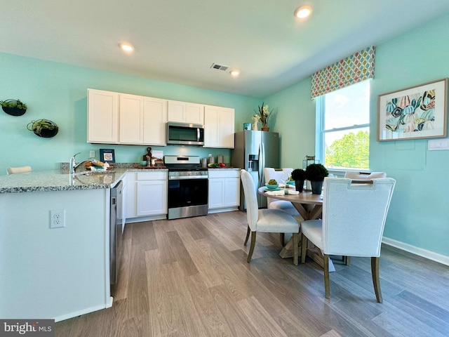 kitchen featuring sink, light wood-type flooring, white cabinetry, stainless steel appliances, and light stone counters