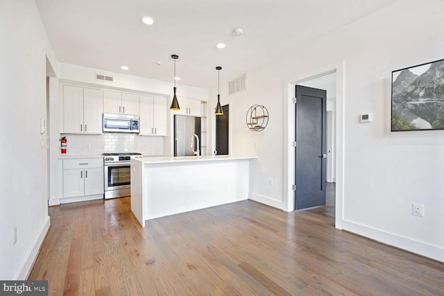 kitchen featuring white cabinets, light hardwood / wood-style floors, decorative light fixtures, and appliances with stainless steel finishes