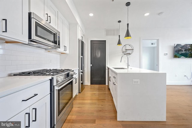 kitchen featuring white cabinetry, appliances with stainless steel finishes, hanging light fixtures, sink, and light hardwood / wood-style floors