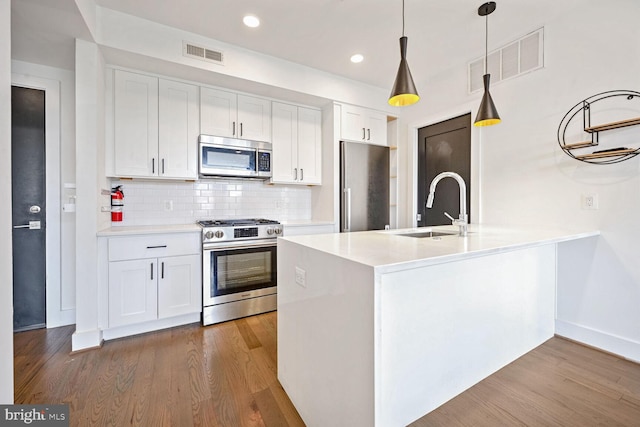 kitchen featuring stainless steel appliances, white cabinetry, sink, decorative light fixtures, and light wood-type flooring