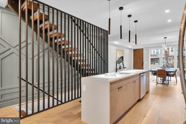 kitchen featuring sink, light brown cabinets, decorative light fixtures, a center island with sink, and light hardwood / wood-style floors