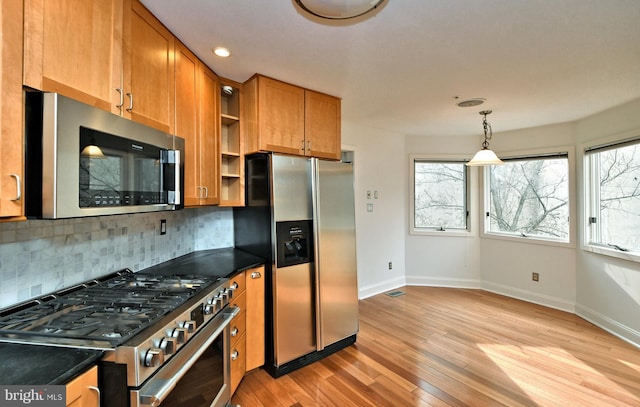 kitchen with light wood-type flooring, decorative light fixtures, backsplash, and stainless steel appliances