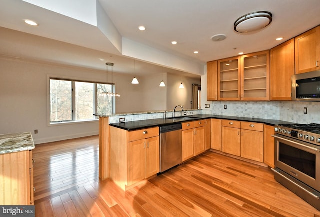 kitchen with kitchen peninsula, dark stone counters, stainless steel appliances, sink, and hanging light fixtures