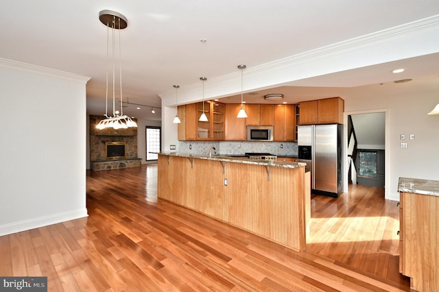 kitchen with kitchen peninsula, appliances with stainless steel finishes, decorative backsplash, a breakfast bar, and a fireplace