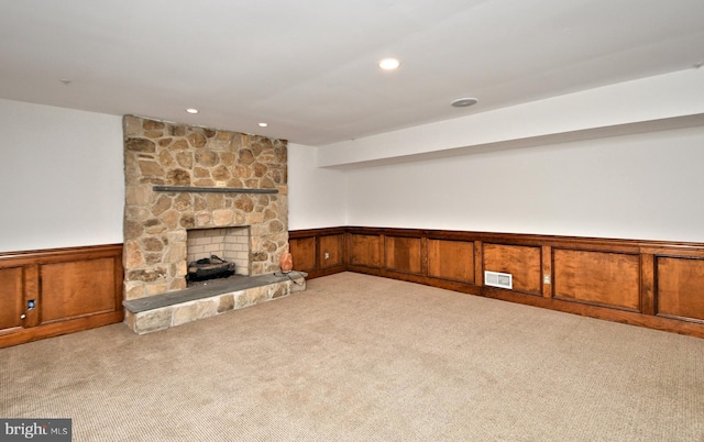 unfurnished living room with light carpet, a stone fireplace, and wood walls