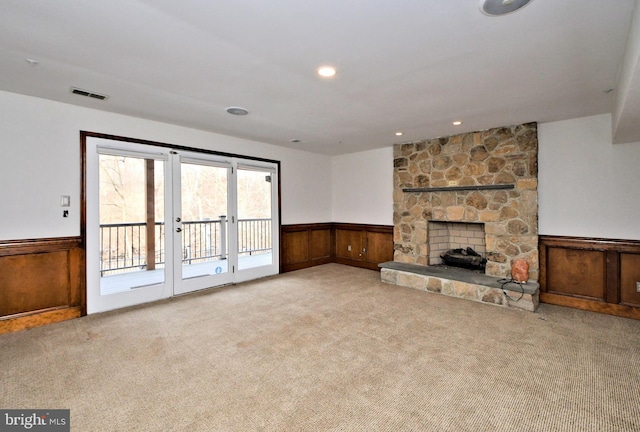 unfurnished living room with light carpet, a stone fireplace, and wood walls